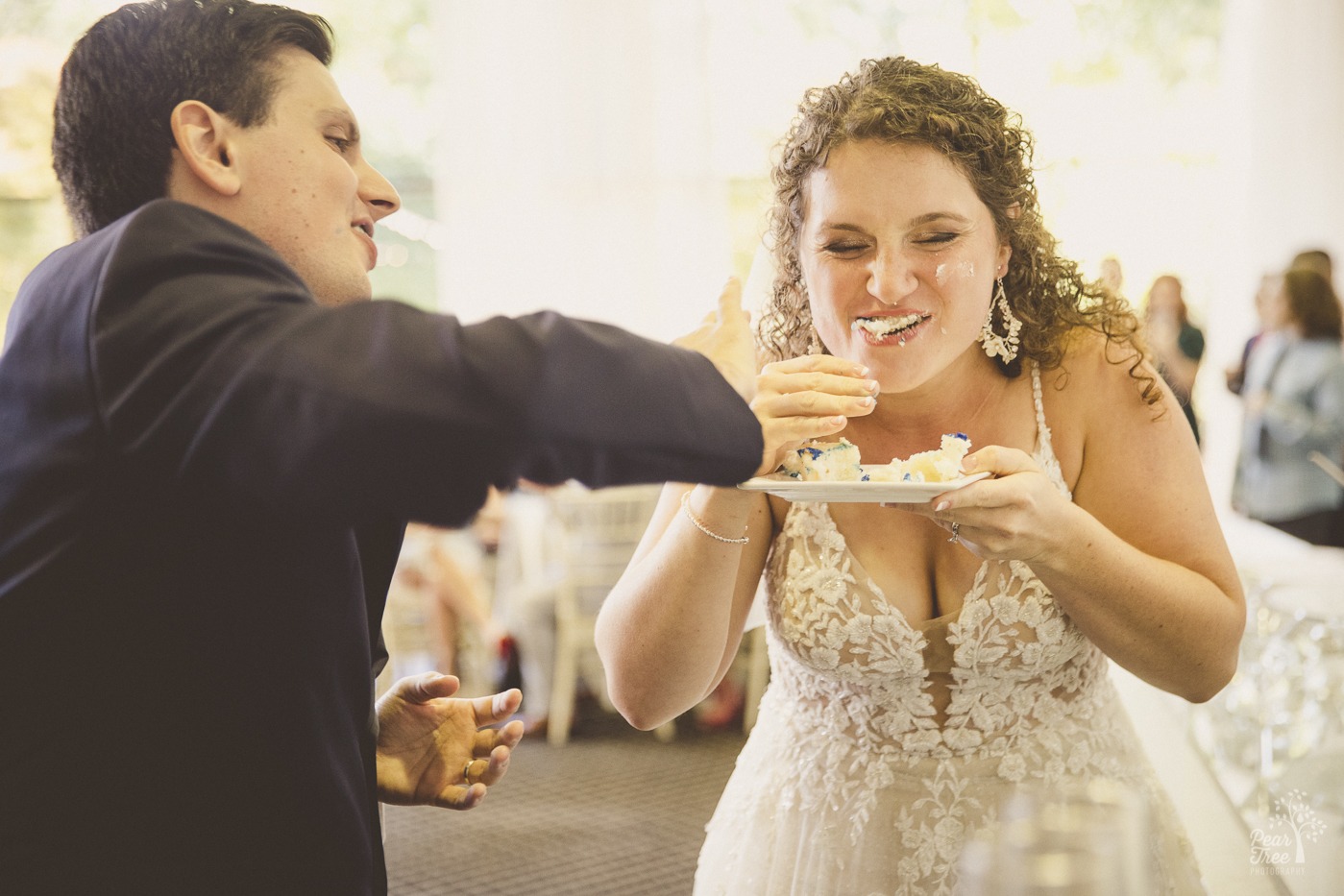 Laughing bride after her groom has shoved cake into her mouth and made a mess of her face at their Atlanta wedding