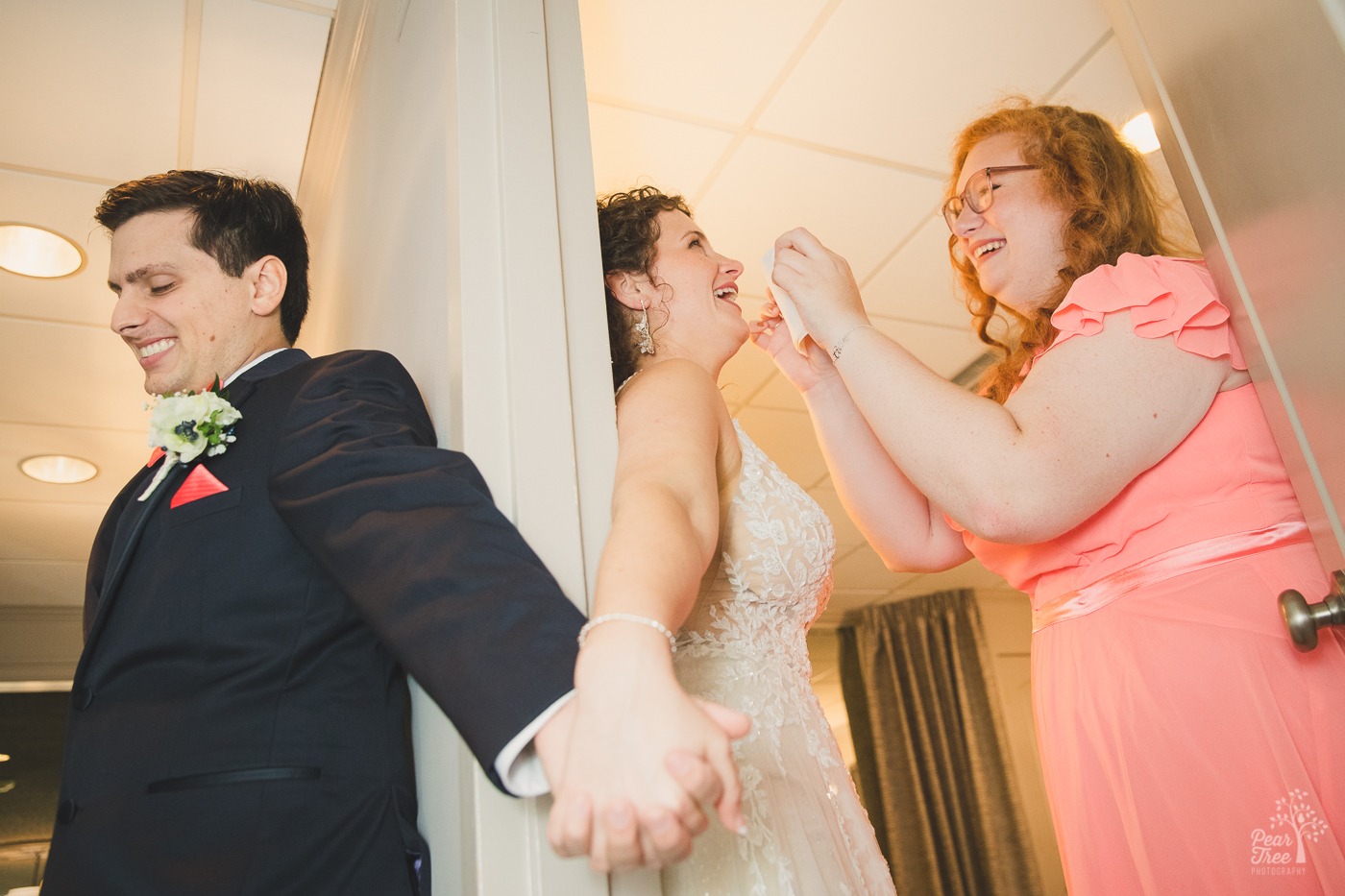 Bridesmaid wiping away bride's tears while she holds her groom's hand around a doorway on her Atlanta wedding day at the Atrium.