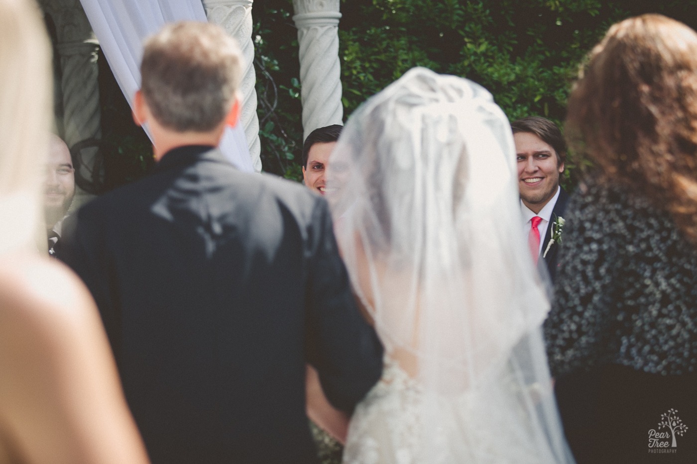 Groom smiling as he watches his wife to be walk down the aisle towards him.