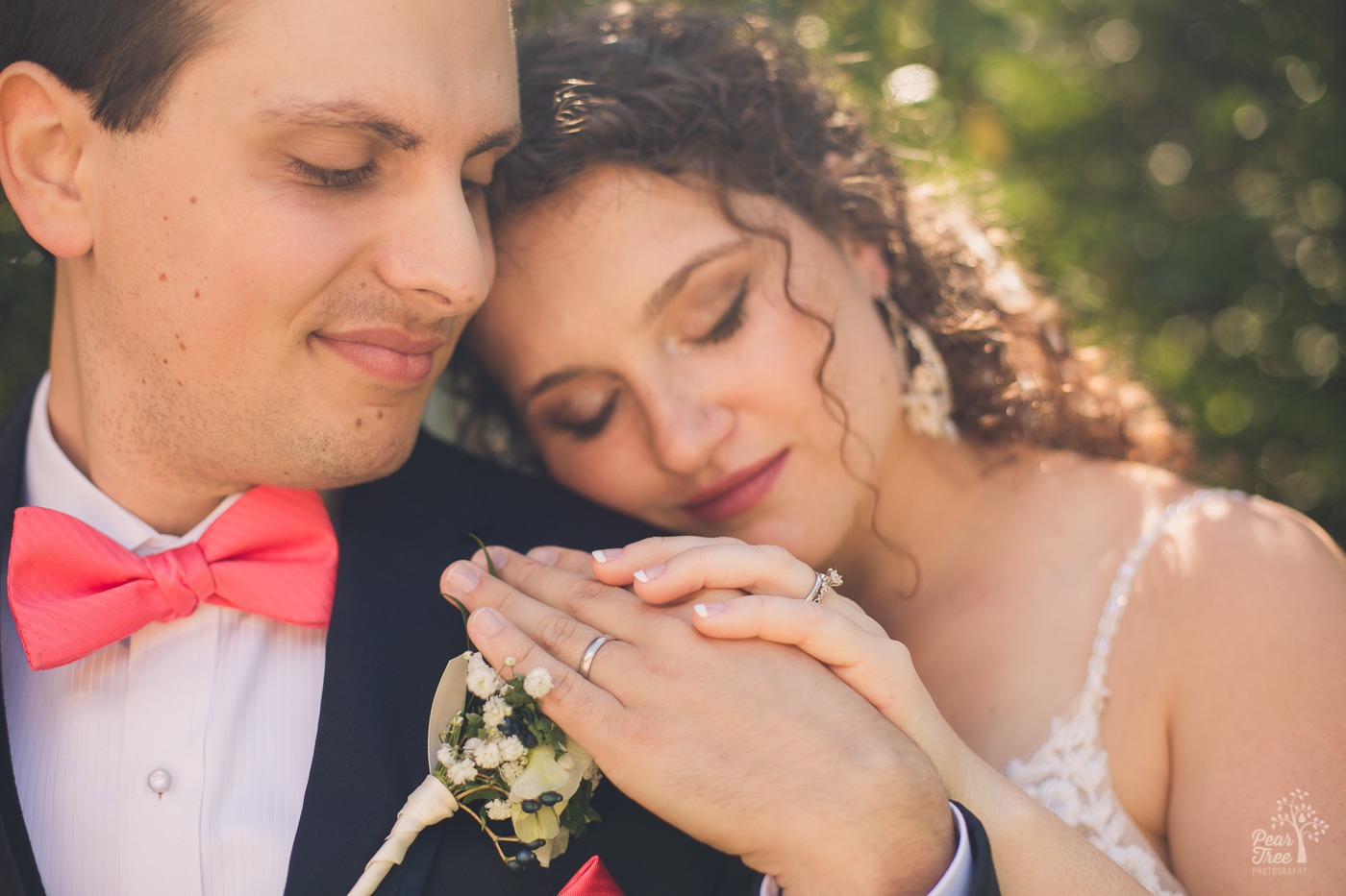 Groom holding his wife's hand on his shoulder while both have their eyes closed while smiling