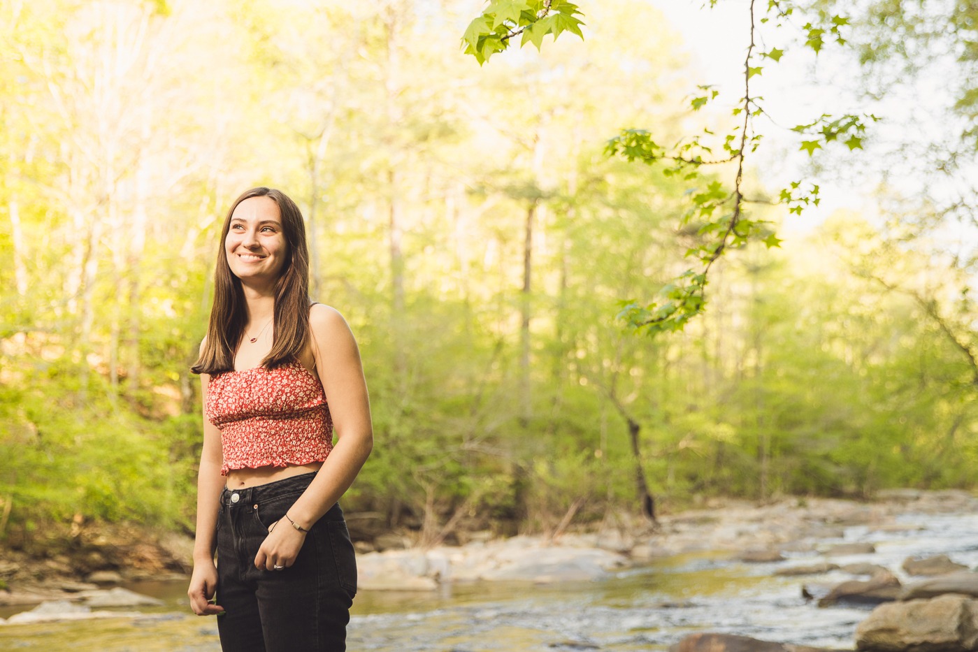 Smiling senior girl with her hand in her jeans pocket and a river behind her