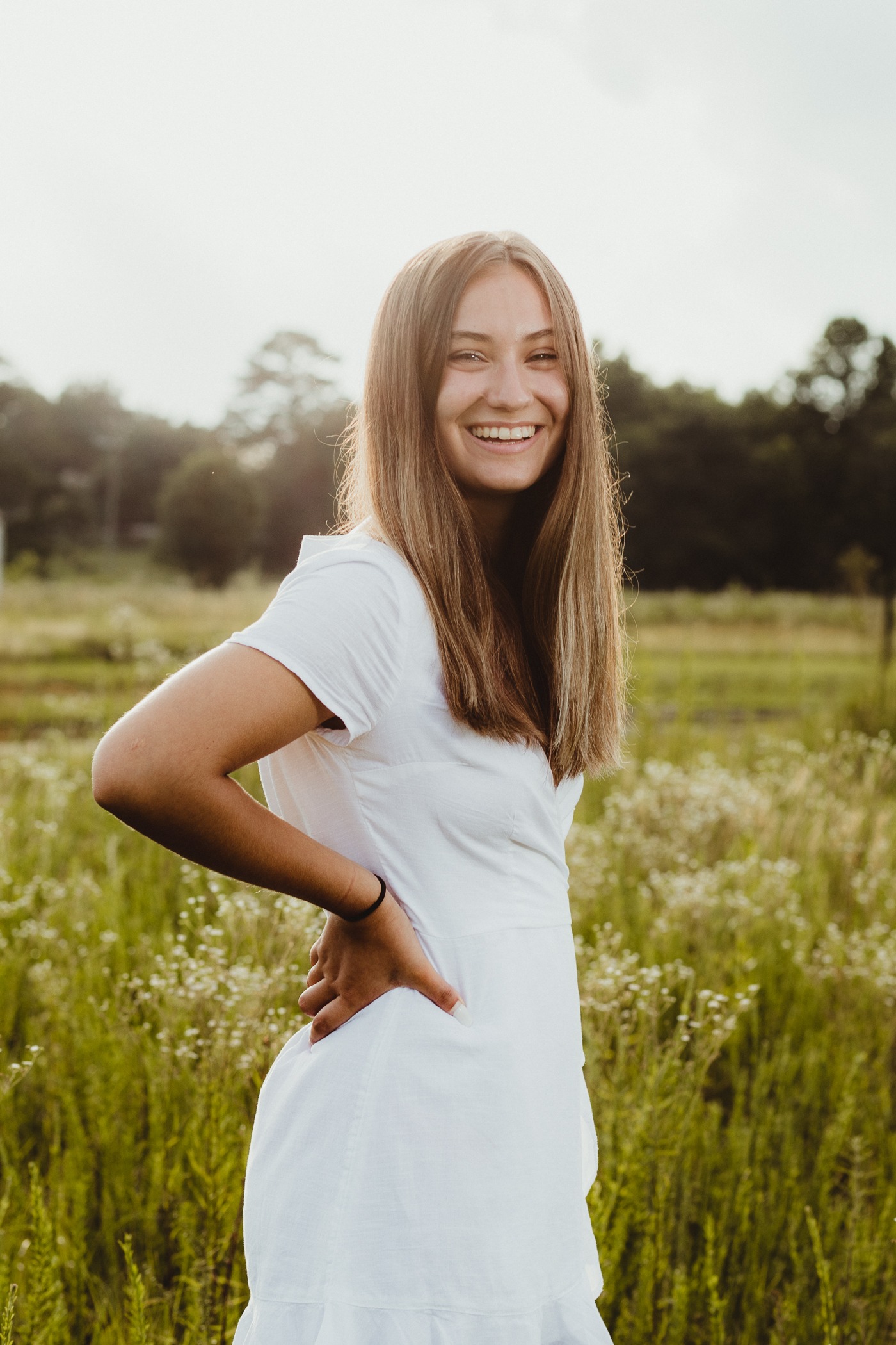 Laughing high school senior girl with hands on her hips wearing a white dress