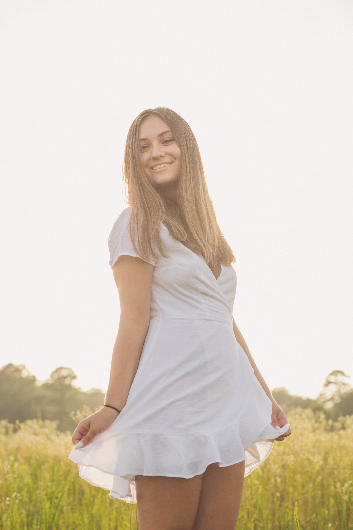 Woodstock high school senior girl fanning out her white dress and twirling in a field of wild flowers