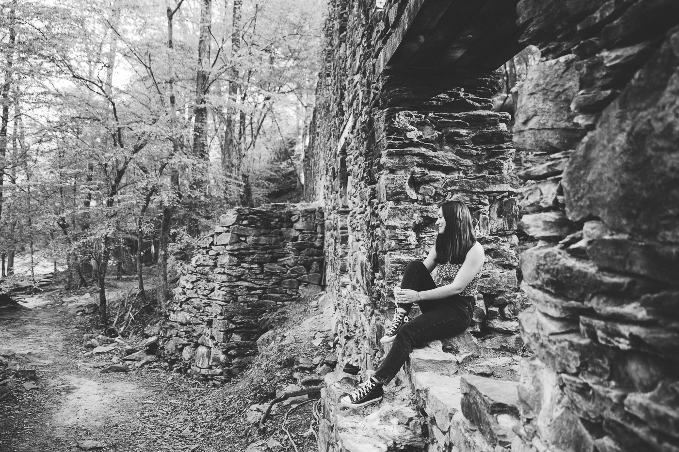 Black and white photograph of high school senior girl sitting in Sope Creek Paper Mill ruins old door opening and smiling