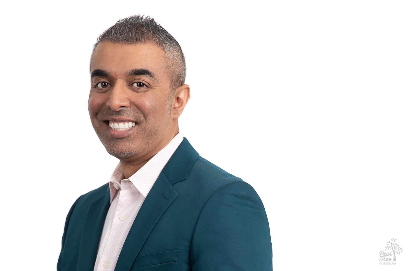 Smiling Indian American male with salt and pepper hair. He's wearing a teal blazer with a light pink button down shirt