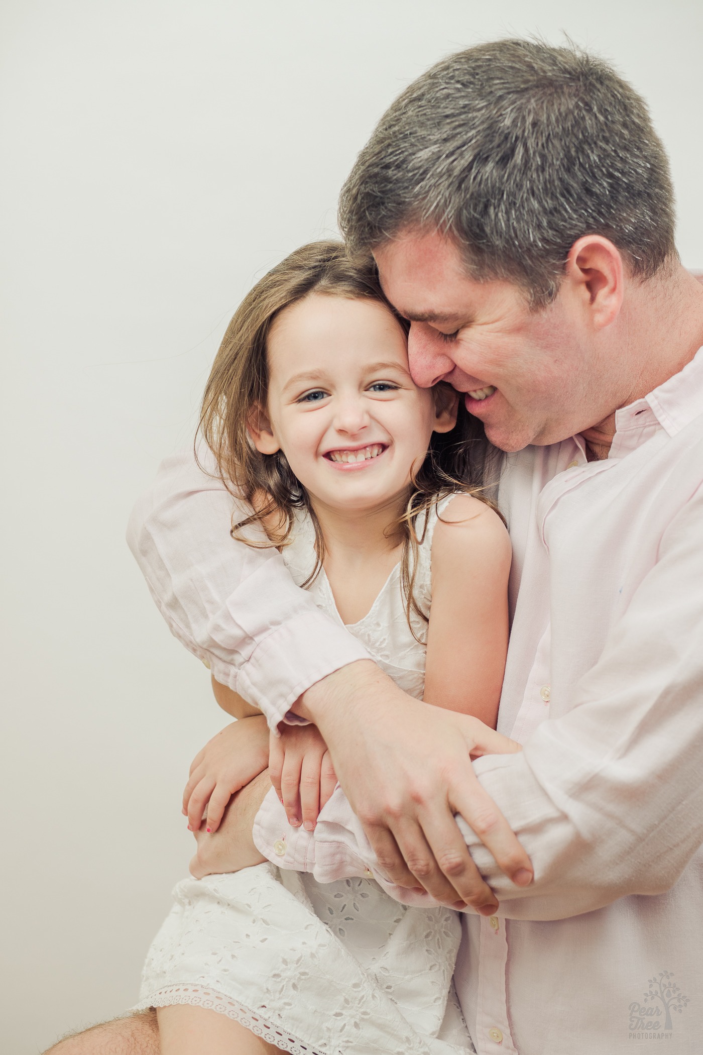 Father nuzzling his daughter's cheek and smiling while hugging her tight