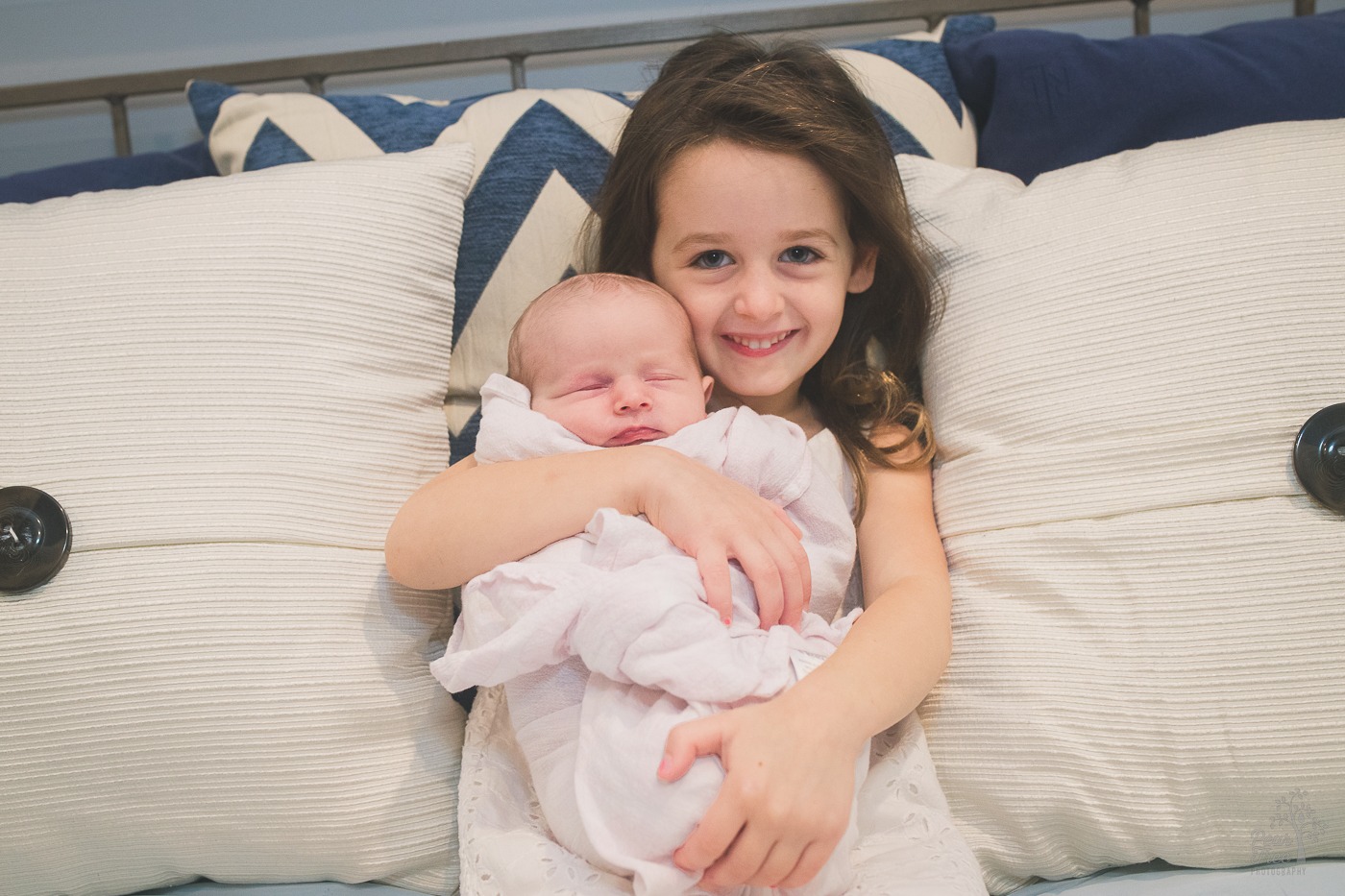 Big sister holding her newborn baby sister and smiling