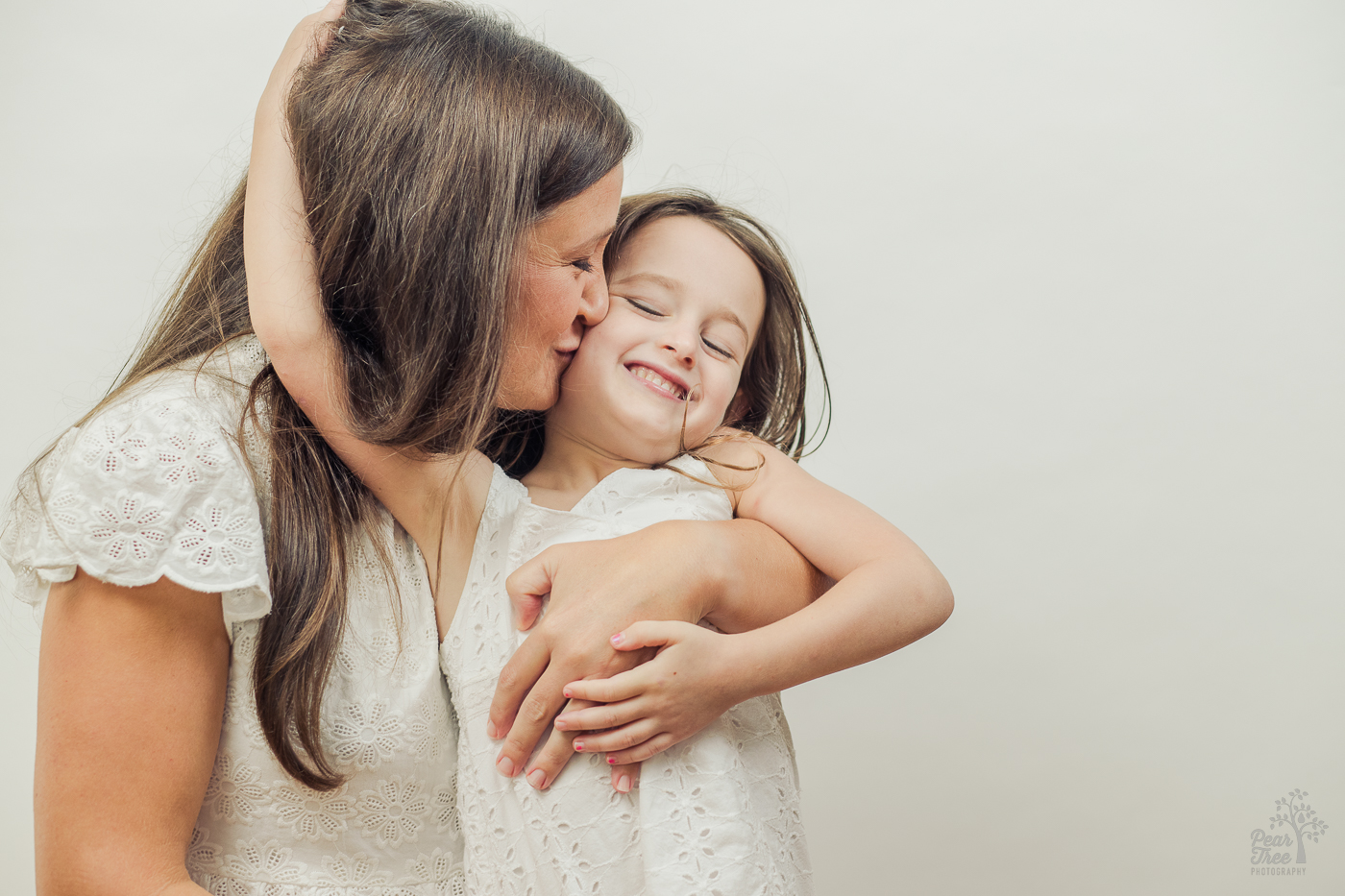 Little girl giggling and grabbing her mom's hair as she's hugged and kissed