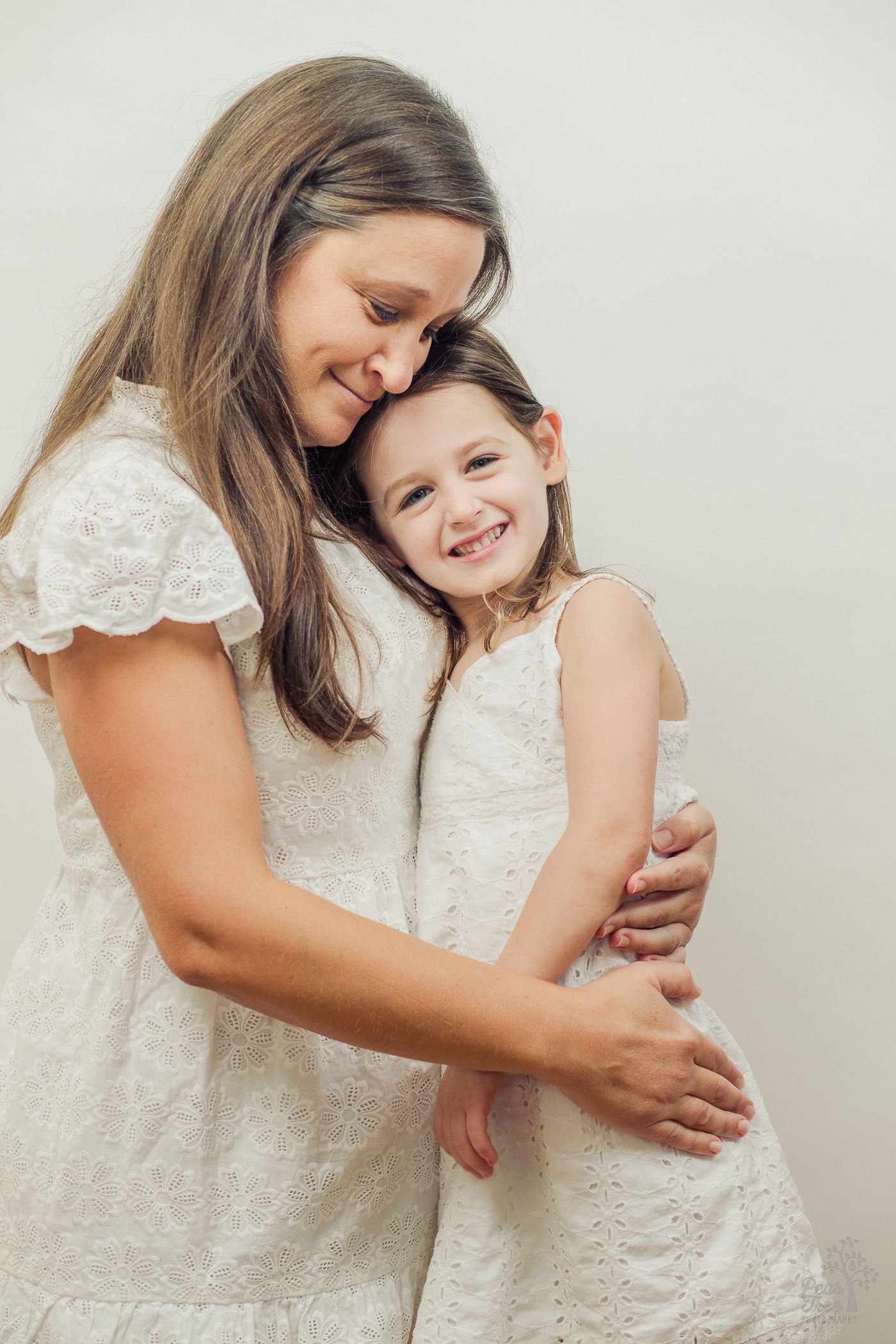 Mom and daughter hugging and smiling while wearing white lacy dresses