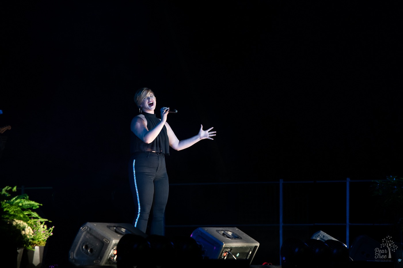 Broadway performer singing on stage with microphone pulling back from her mouth in one hand and her other hand outstretched