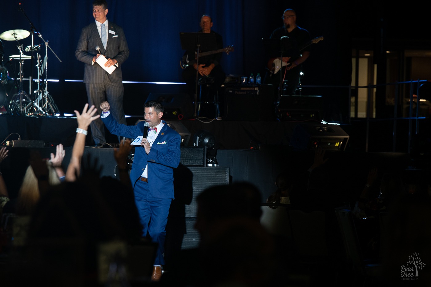 Auctioneer revving up crowd for fundraising the Night of Broadway Stars with Clark Dean smiling on stage smiling behind him