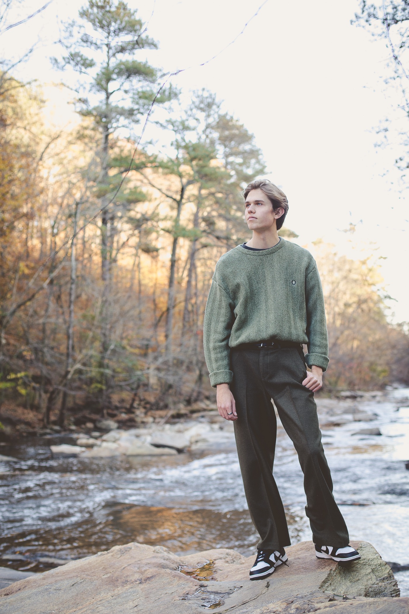 High school senior boy wearing a green sweater and looking at woods in Sope Creek
