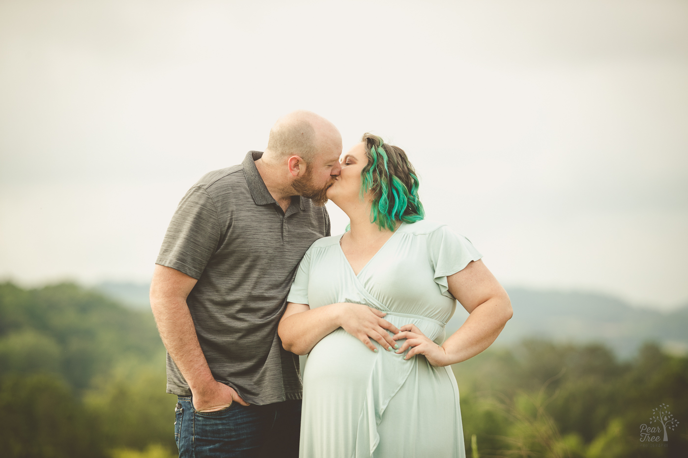 Pregnant couple kissing for maternity photographs in a Cartersville field