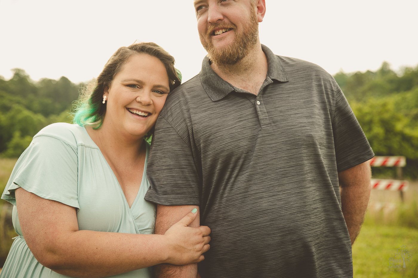 Laughing woman in a green dress and teal hair holding her husband's arm while he smiles