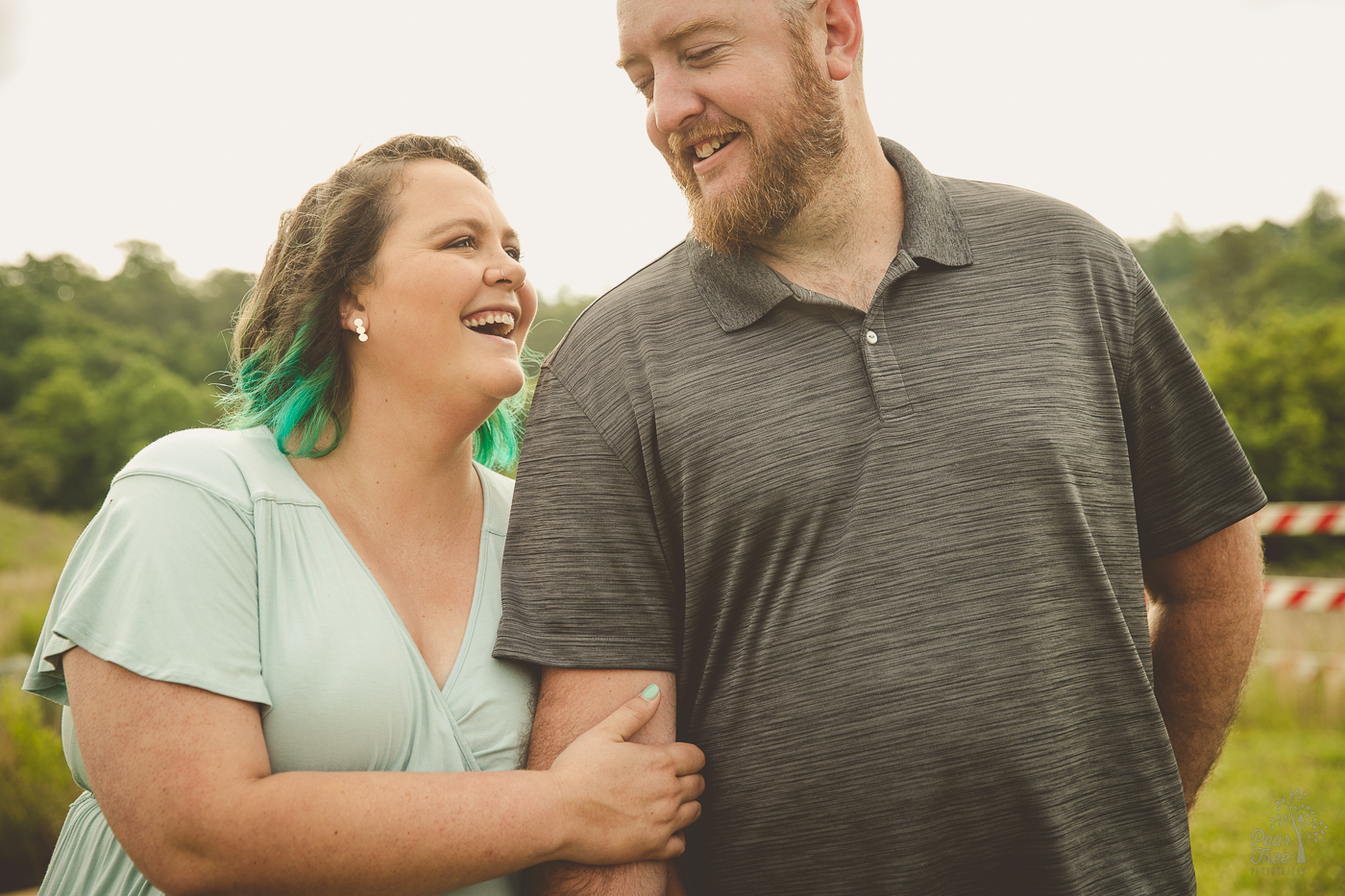 laughing couple holding each other close. The woman is wearing a green dess and nail polish with teal hair