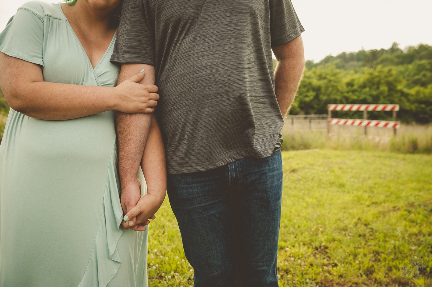 Photograph of pregnant couple leaning on each other with arms intertwined. Their faces can not be seen