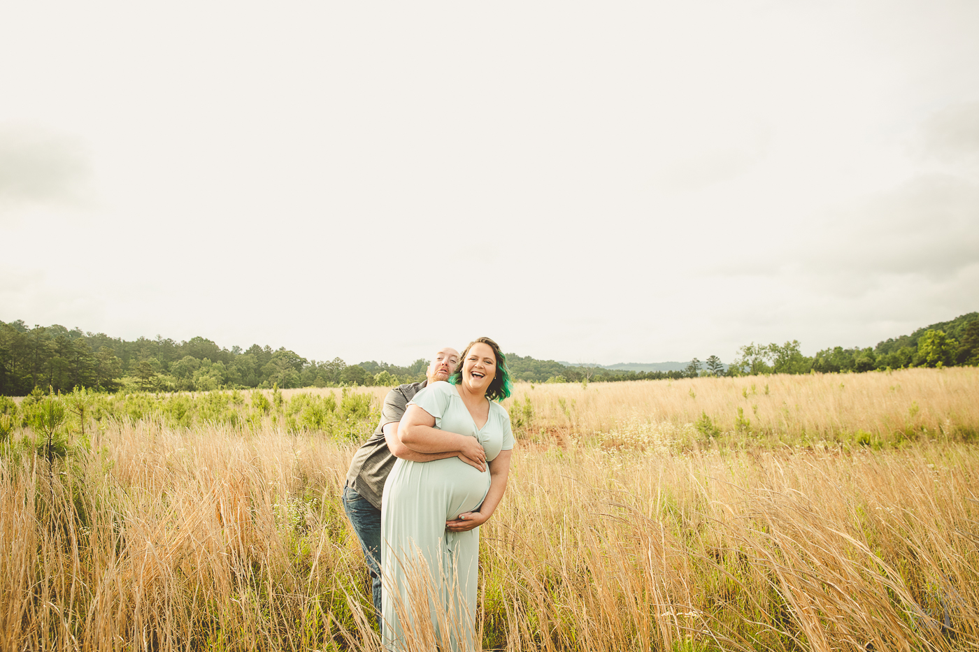 Pregnant couple goofing around making funny faces and laughing in a field for maternity photographs