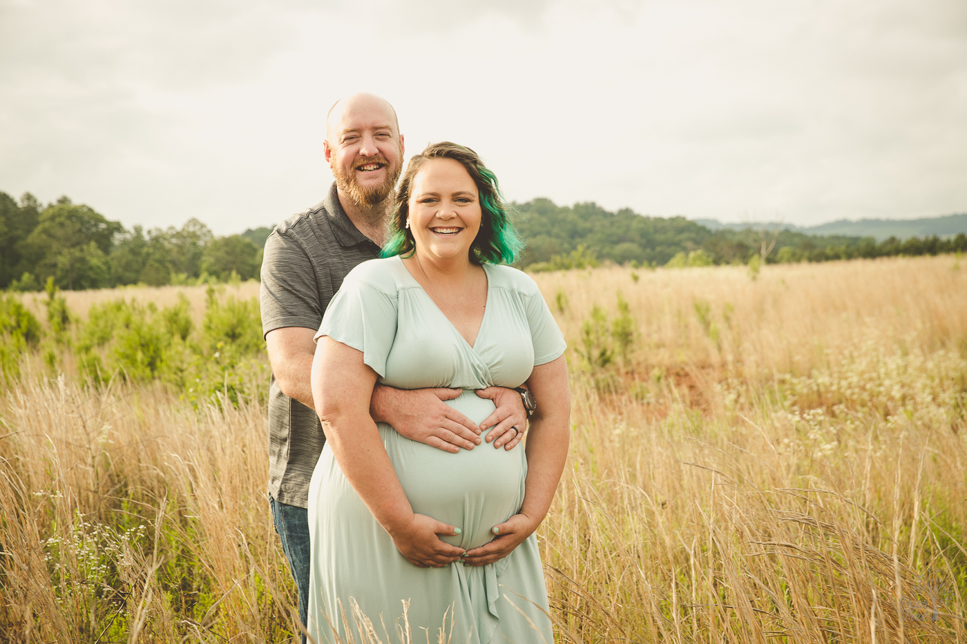 Pregnant mom holding her big belly. Her husband standing behind her with his hand forming a heart on top of her belly for maternity photographs
