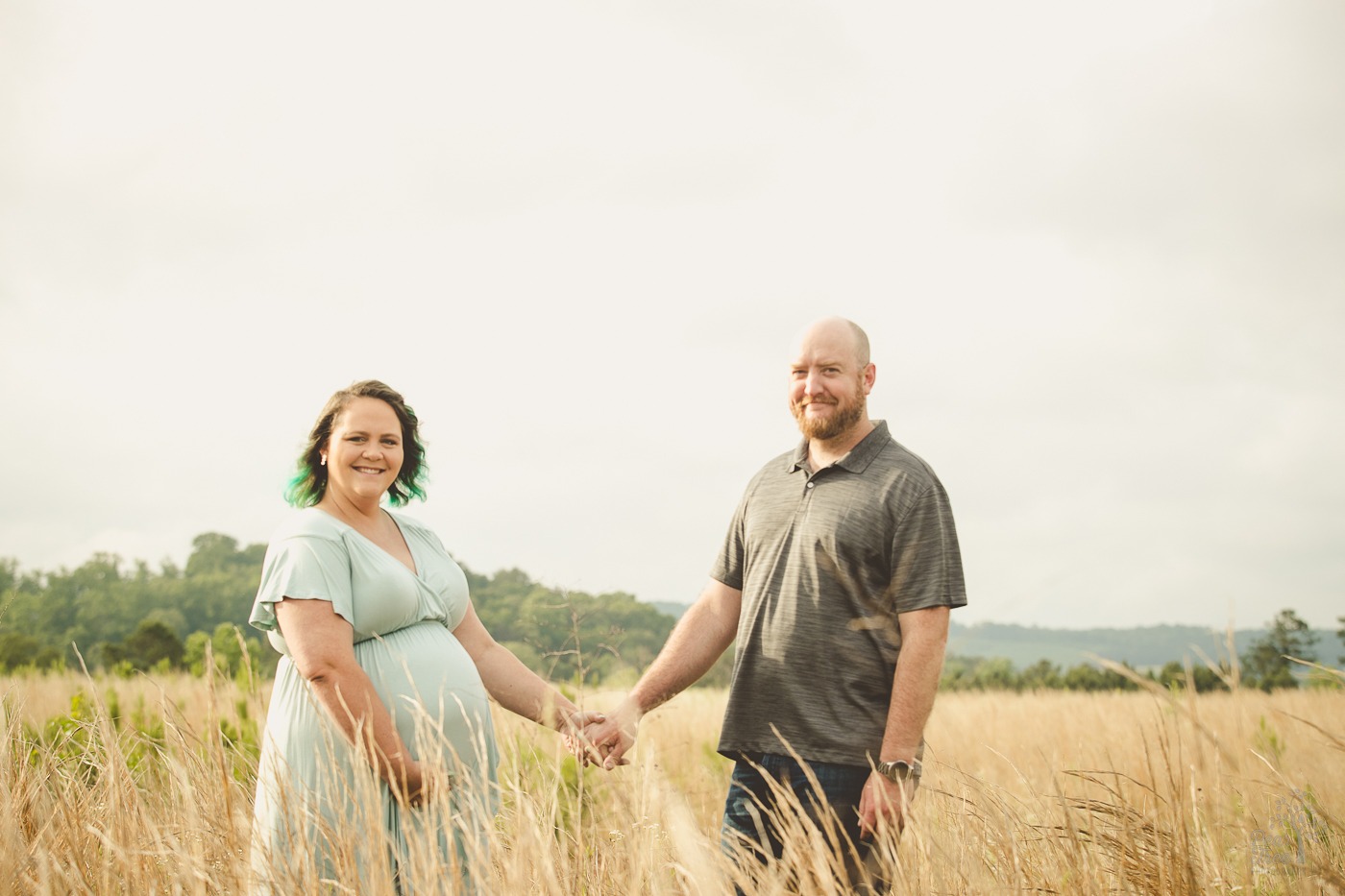 Expecting parents standing in a field of tall grass holding hands and smiling for maternity photos