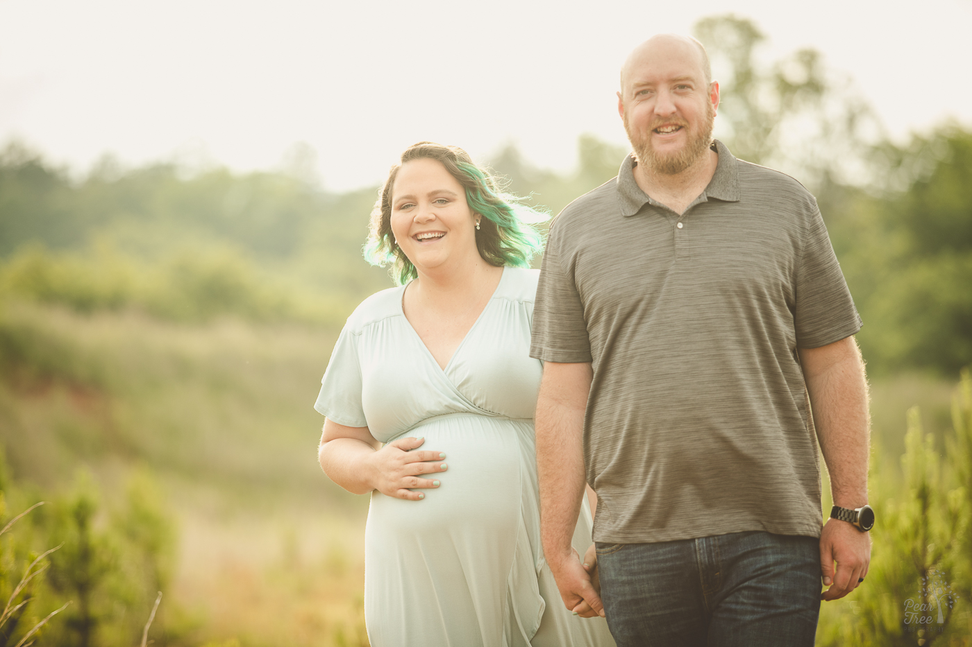 Pregnant couple holding hands and walking toward the camera smiling big