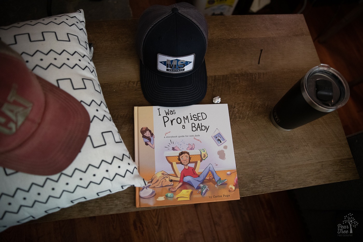 The book "I WAS PROMISED A BABY" sitting on a coffee table next to two hats and a coffee mug