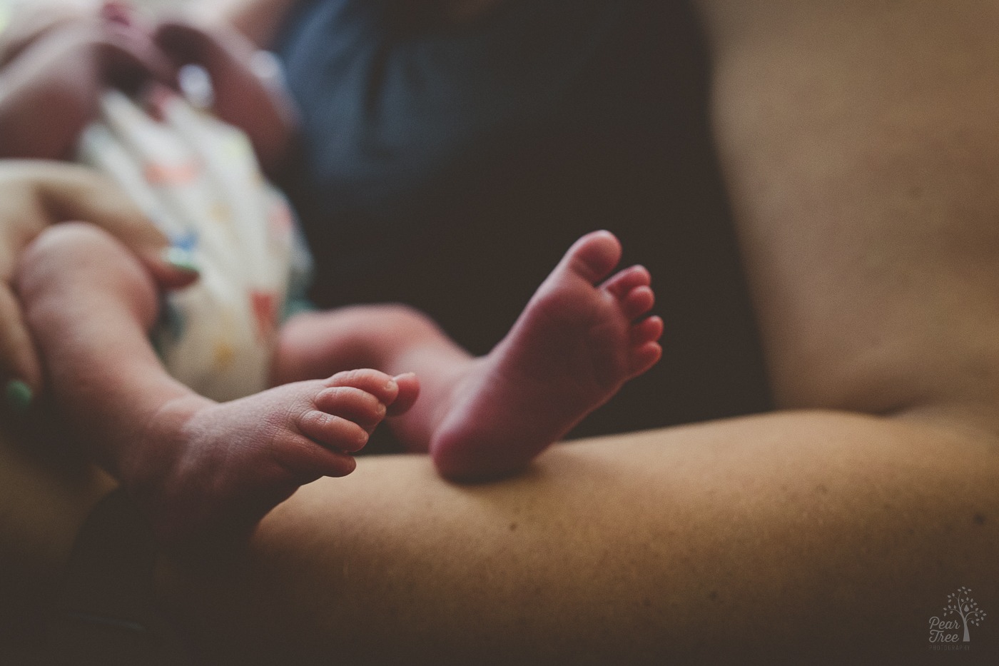 Newborn feet extending over his mama's arms
