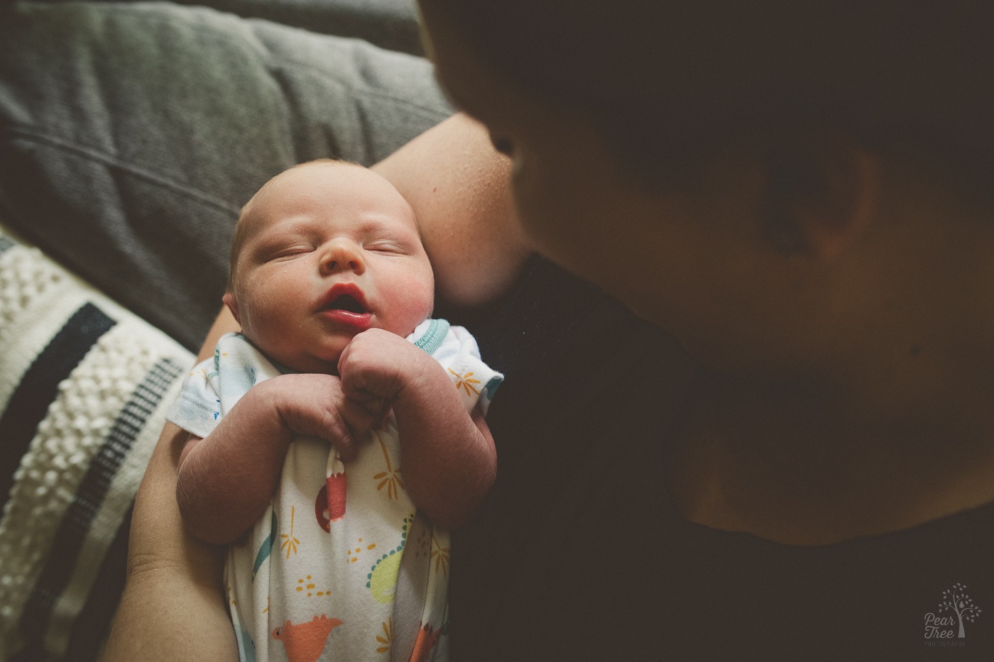 Newborn baby boy being cradled in his mom's lap and arms with his hands held close together