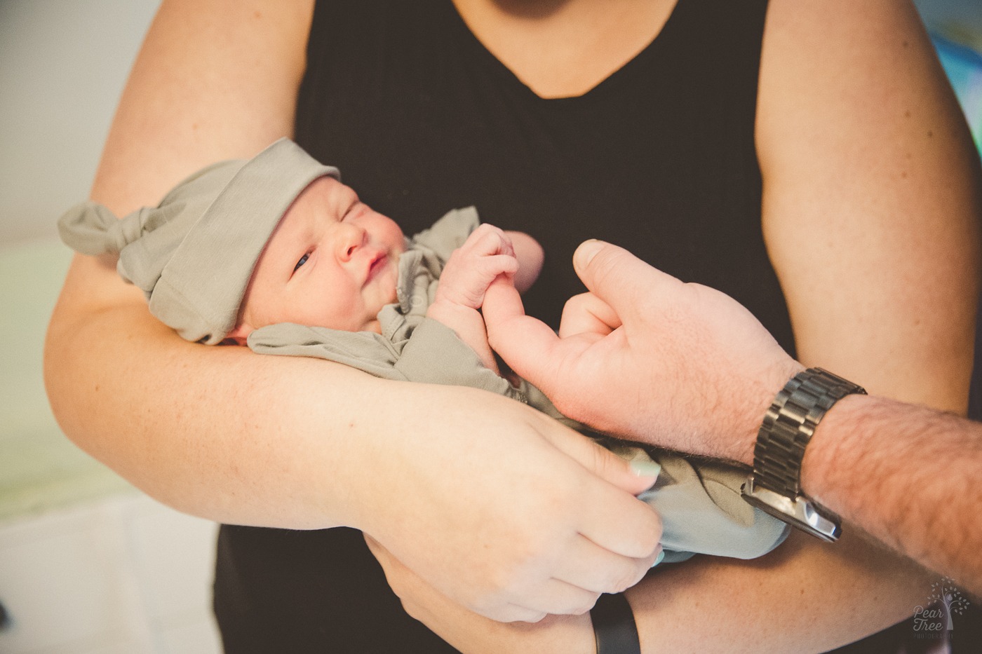 Mom holding her newborn son while dad let's baby grasp his finger