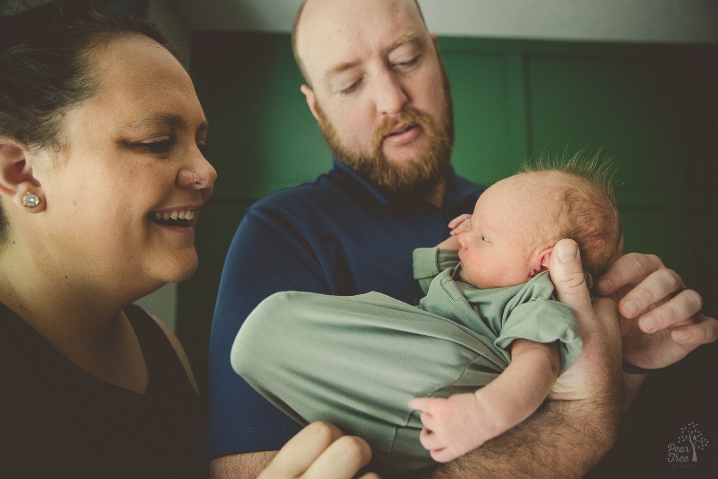 parents holding their newborn son and enjoying the mohawk they created with his hair