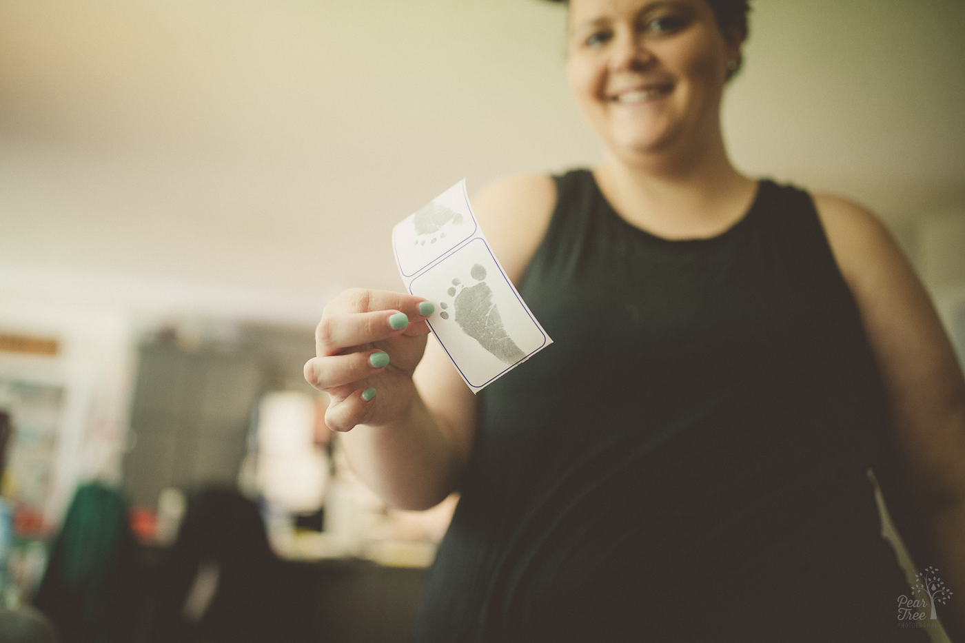Smiling mom holding up her son's footprint during her newborn photography session.