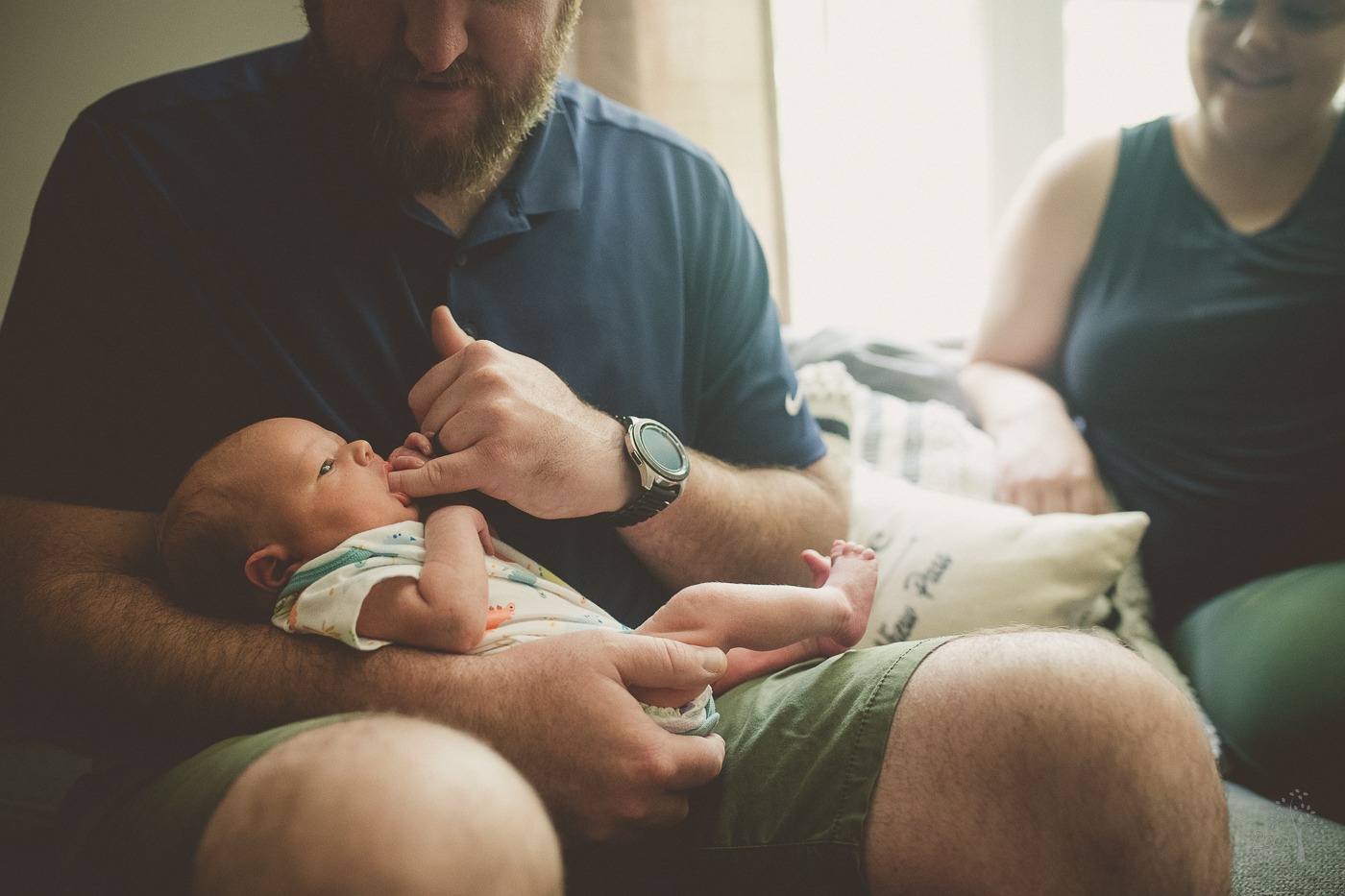 Newborn son sucking on his dad's pinky finger while being held by dad