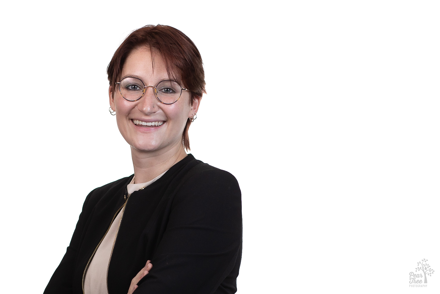 Caucasian woman wearing a black zipper jacket, small hoop earrings, and glasses smiling for a professional headshot