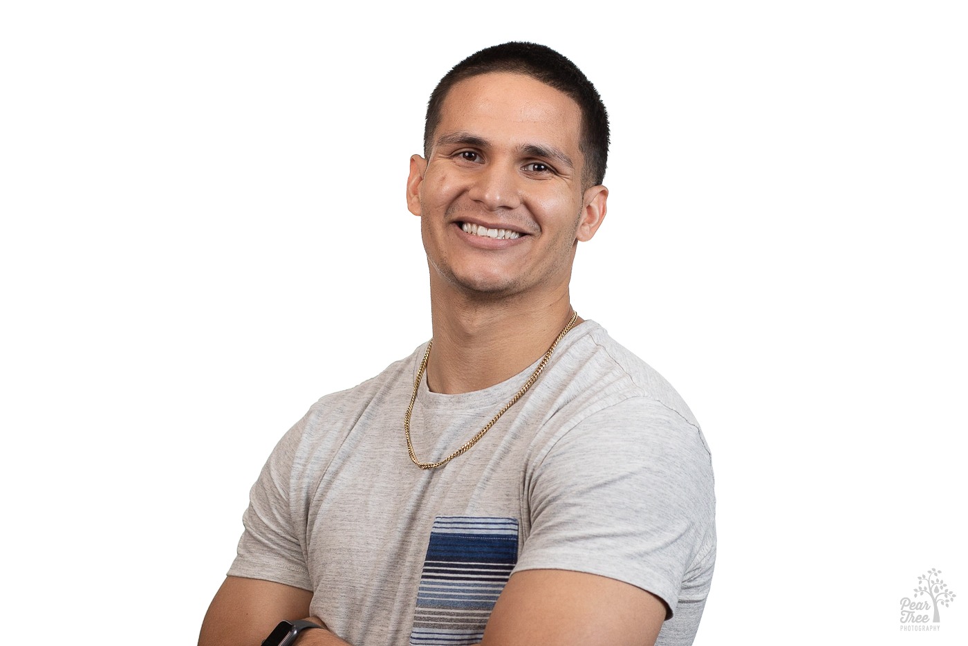 Latin American man wearing a grey tshirt, black Apple watch, and gold chain smiling for a professional headshot in Atlanta front of a white backdrop
