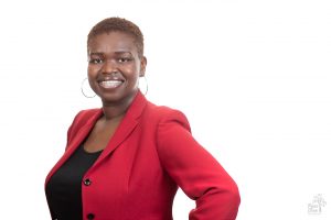 Attractive and smiling African American woman wearing a black blouse and stunning red blazer with big gold hoop earrings and braces for a professional headshot