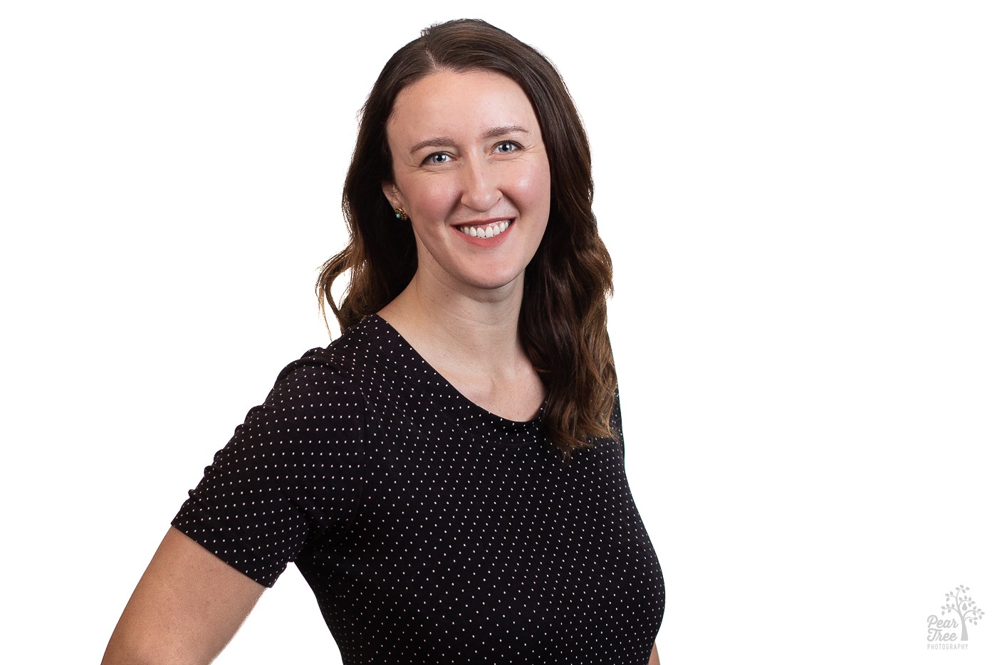 Attractive Caucasian woman with long, wavy brunette hair wearing a black with white pin polka dot short sleeved shirt smiling for a professional headshot