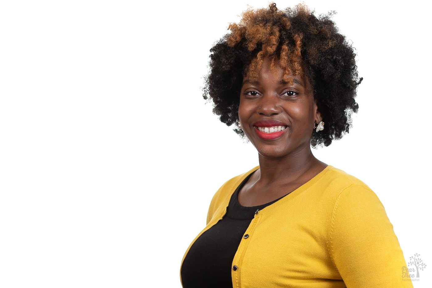 African American woman wearing red lipstick and a yellow cardigan over a black blouse is smiling for a professional headshot in Atlanta front of a white background