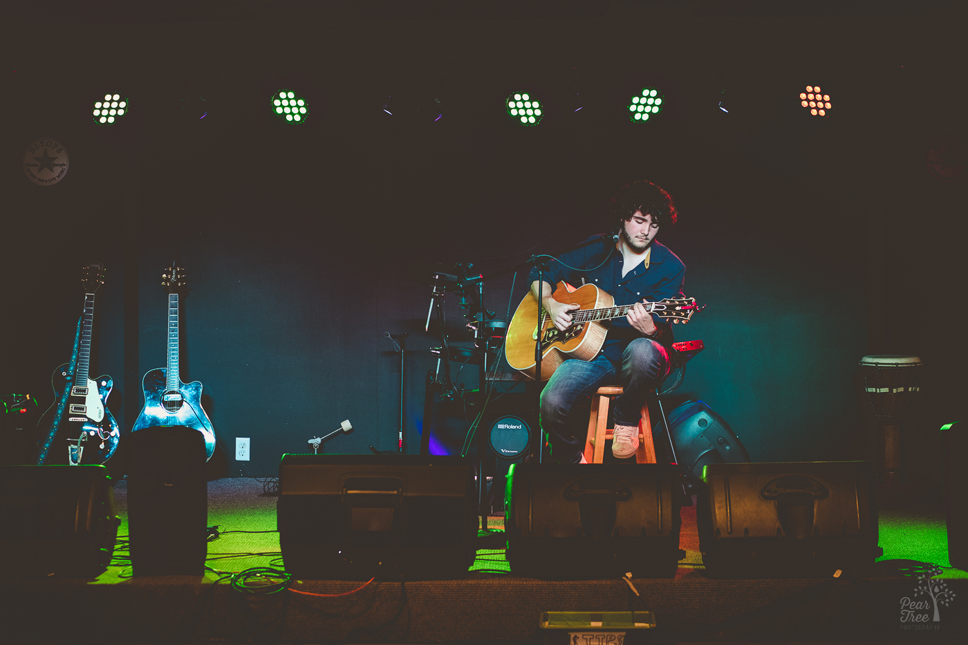 Hunter Rose sitting on a stool playing his guitar under stage lights