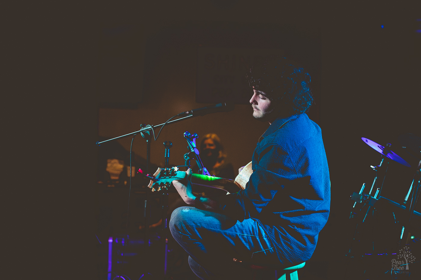 Hunter Rose playing his guitar on stage under white, green, and purple lights