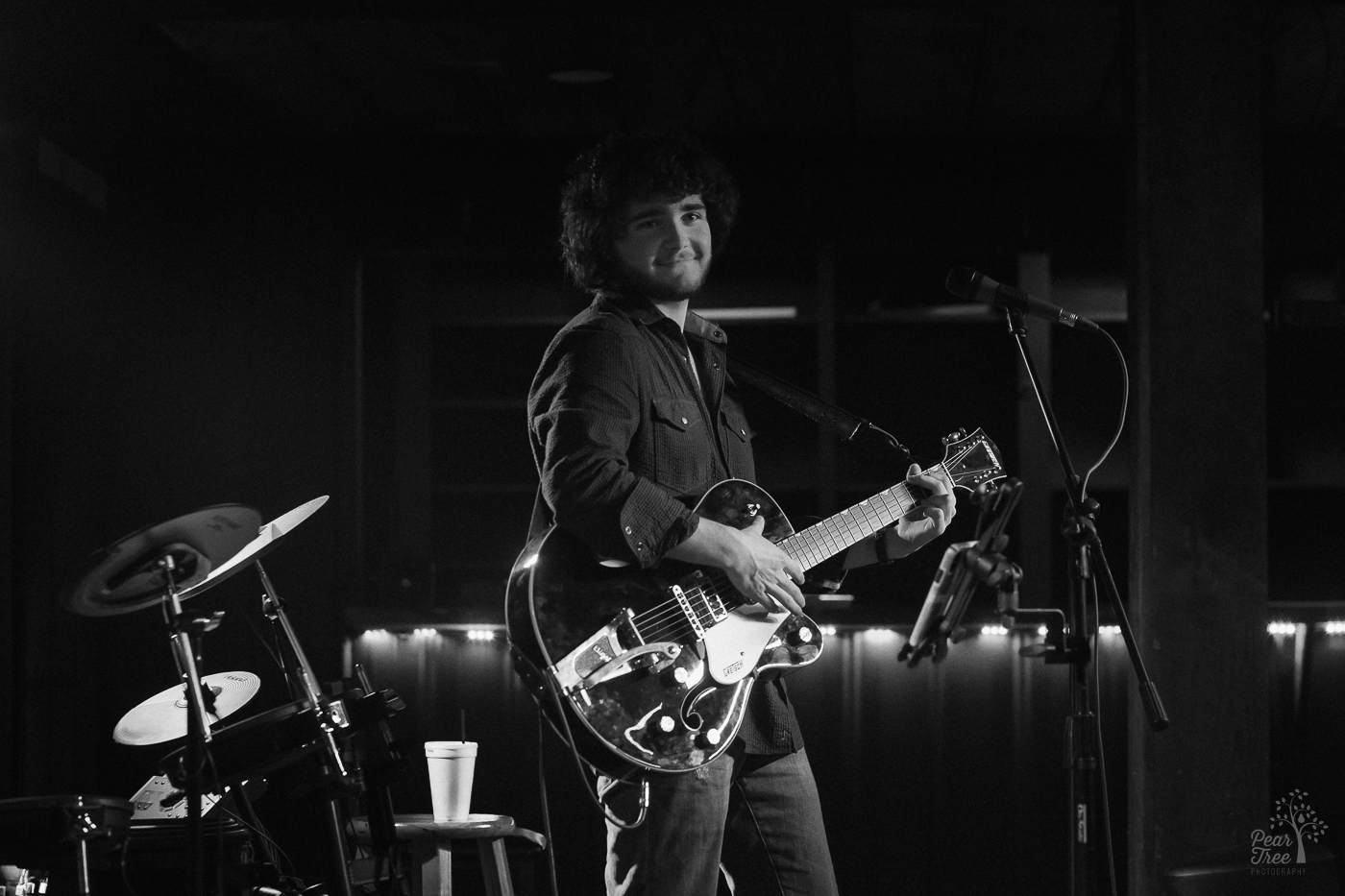 Black and white photograph of Hunter Rose holding his guitar on stage and smiling