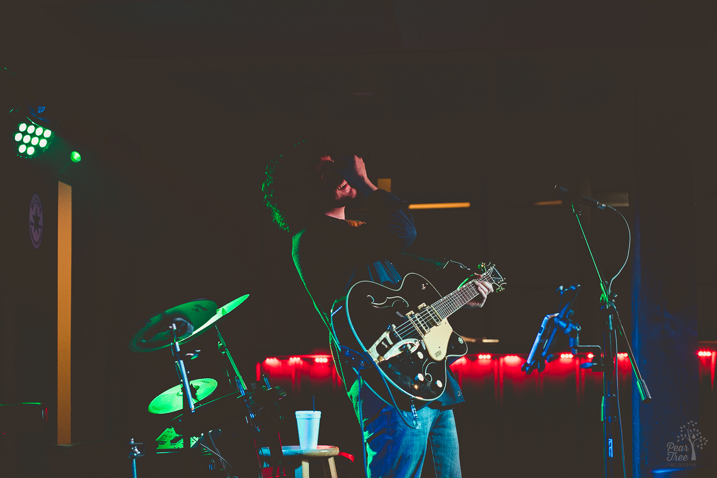 A singer leaning backwards into the shadows and laughing while covering his face