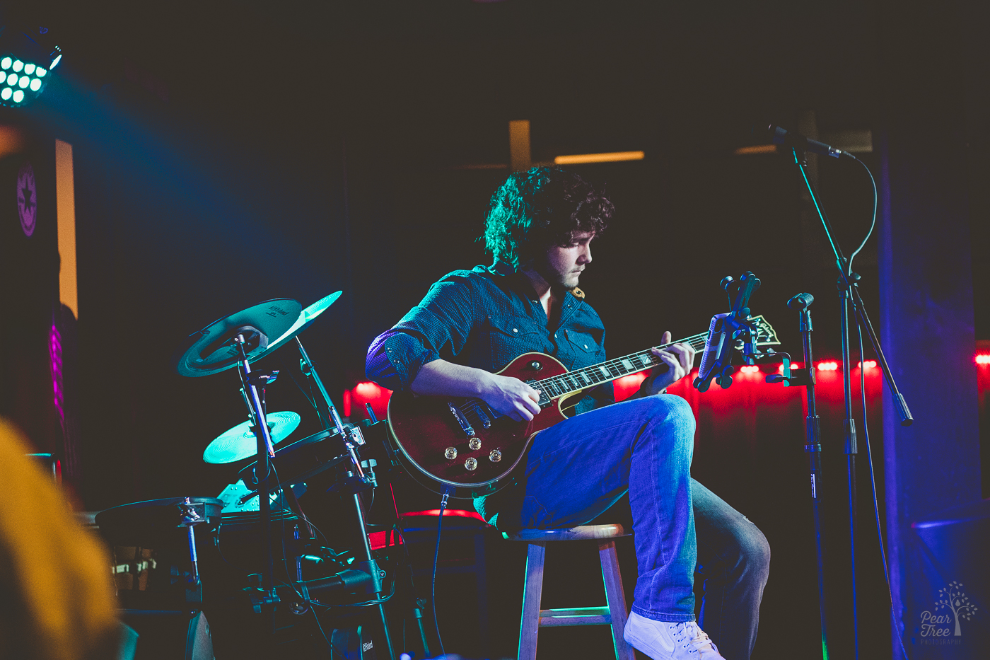 Hunter Rose sitting on a stool on stage and playing an electric guitar