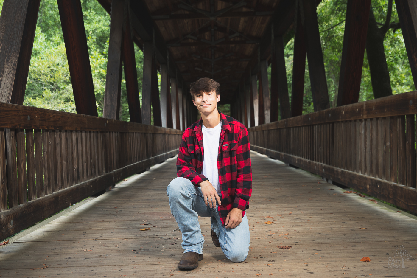 High school senior boy kneeling on Roswell Mill covered bridge and smiling
