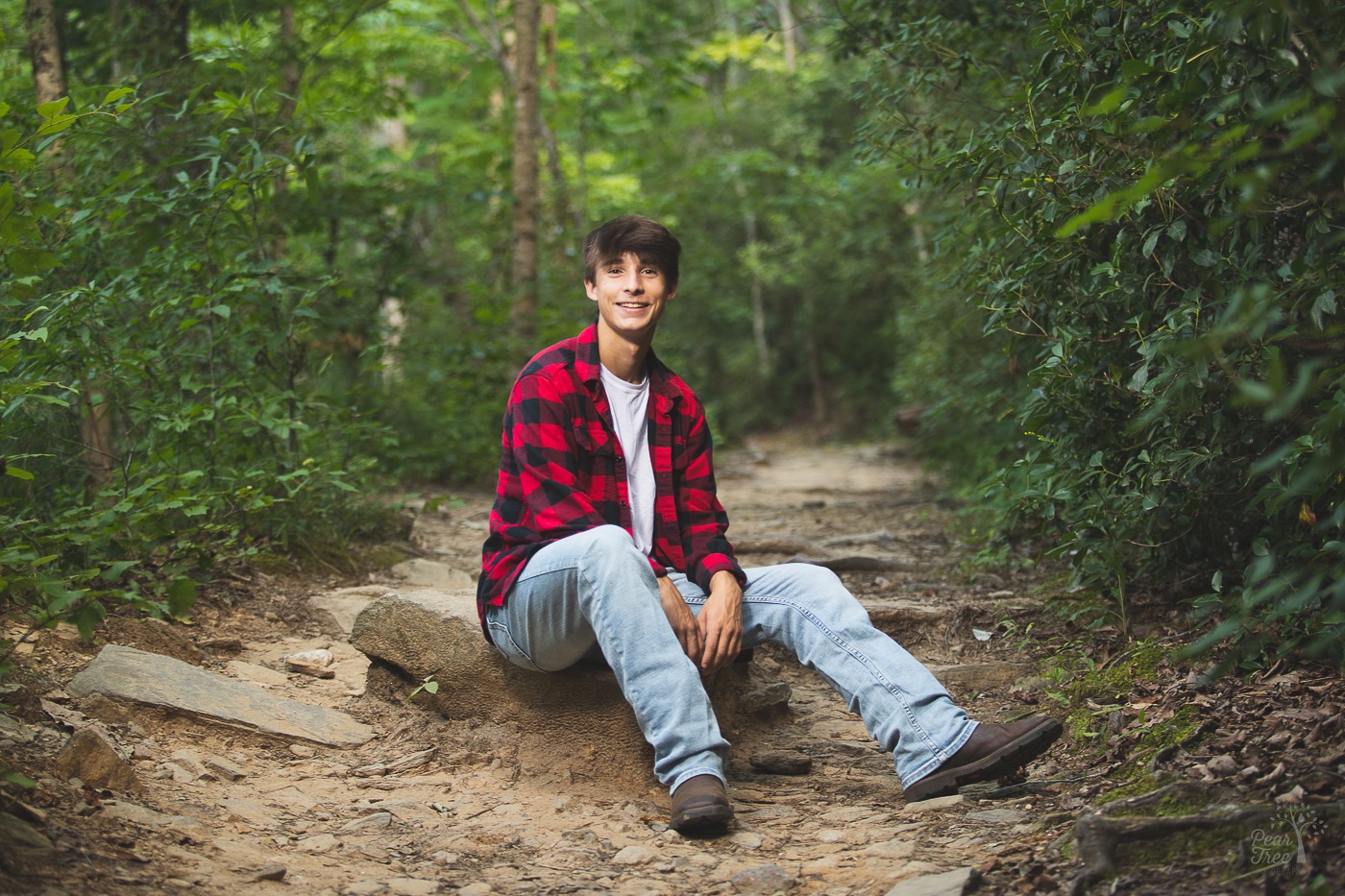 High school senior boy sitting on rocks in the middle of Roswell Mill Trail