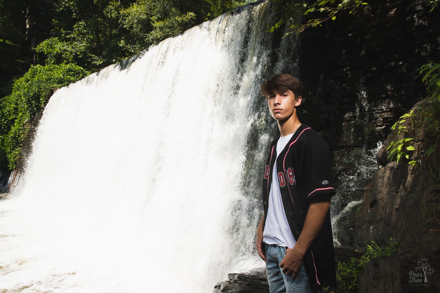 High school senior boy standing with thumbs in pockets at bottom of Roswell Mill dam