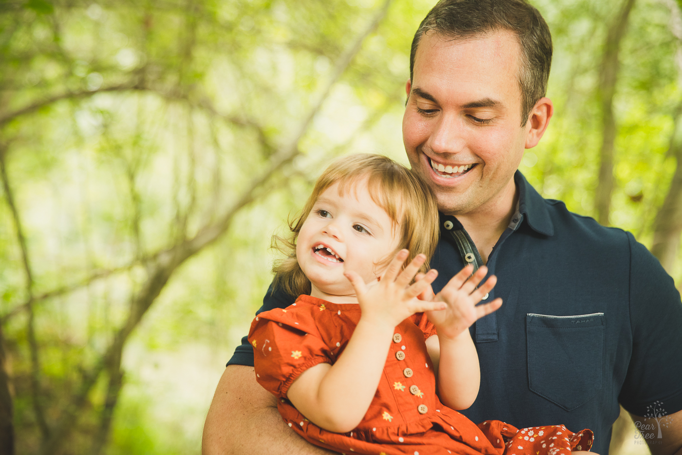 Dad holding his youngest daughter close and laughing while she smiles and claps happily