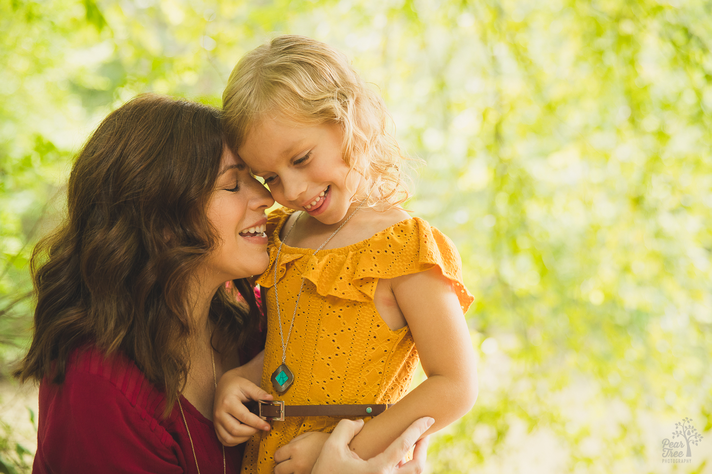 Beautiful mom with wavy hair nuzzling her oldest daughter and hugging her close while the two smile