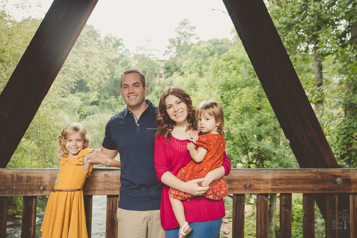 Sweet family standing together in Roswell Mill covered bridge with mom holding the littlest girl and the older one smiling next to dad.