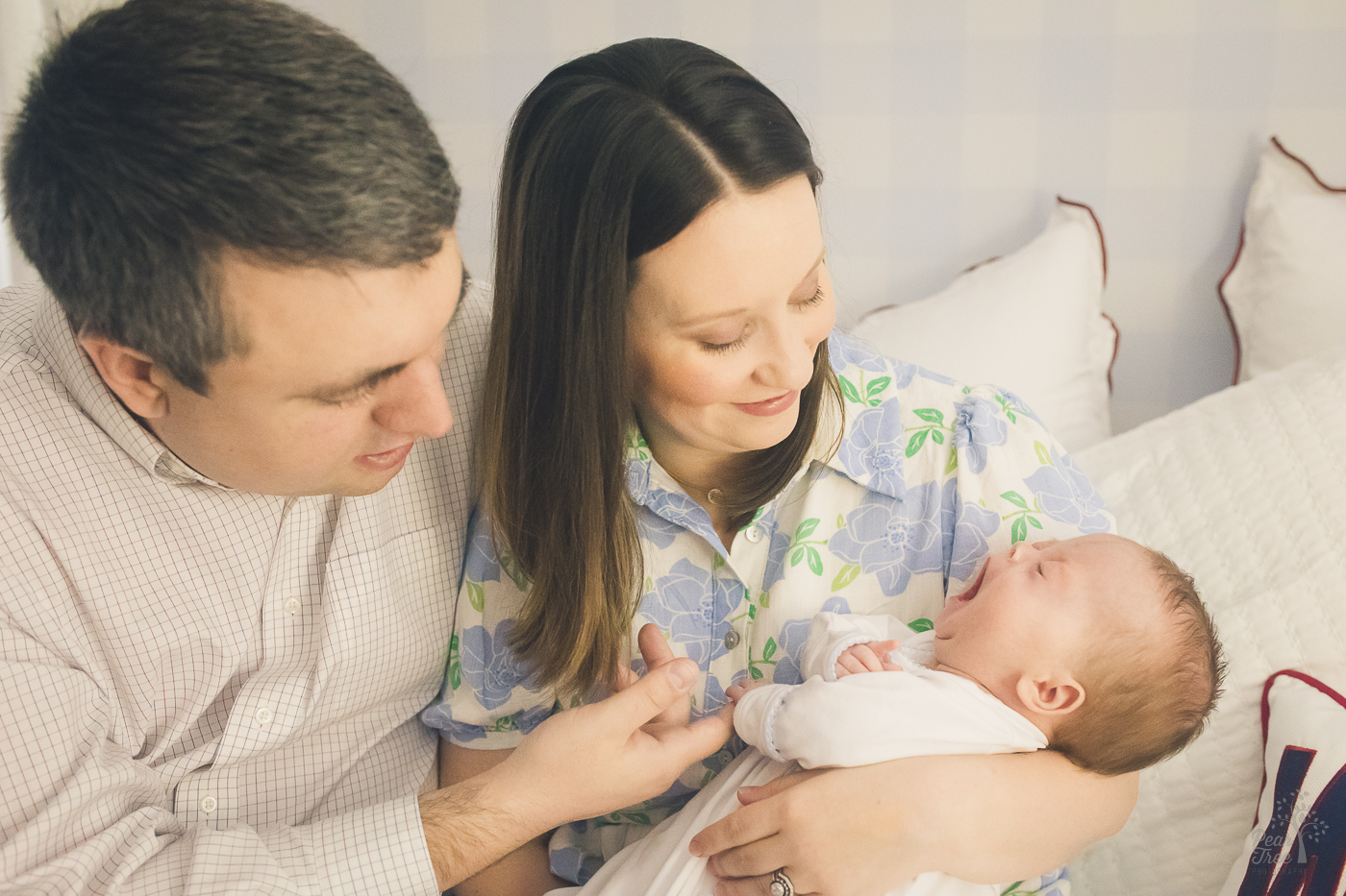 Dad is letting his son hold his finger. Mom is holding the baby while he yawns big during newborn photographs.