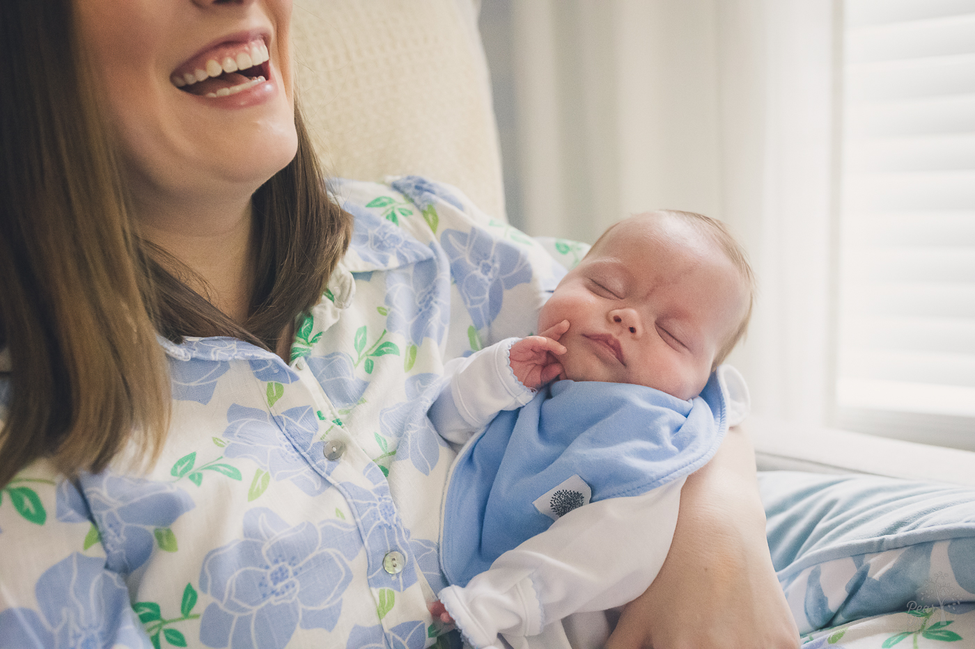 New mom is laughing while holding her sleeping newborn baby boy with his hand on his cheek