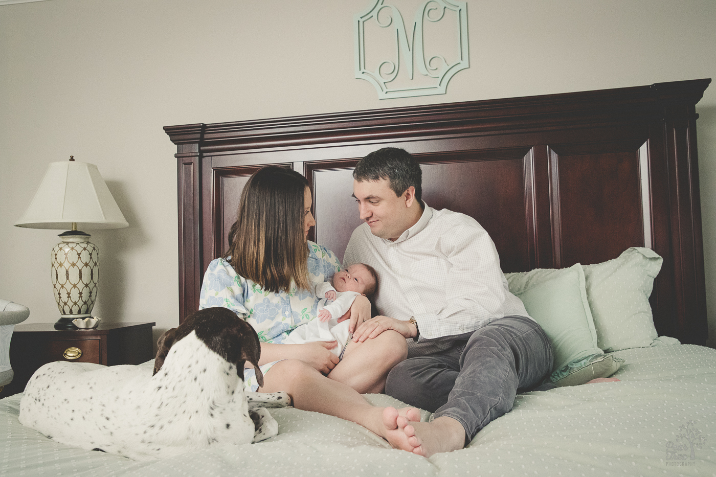 New parents sitting on the master bed with the family dog and their newborn baby boy